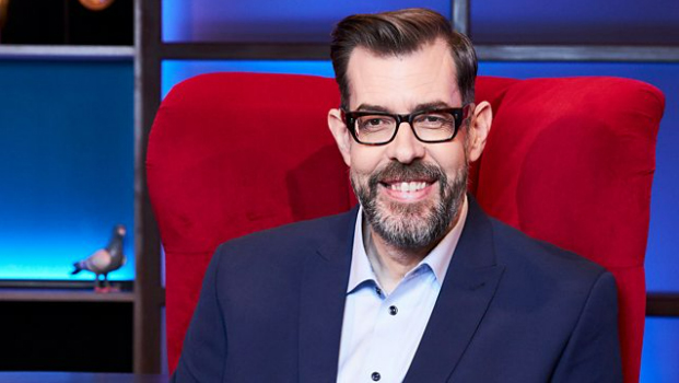 a man with a beard and glasses is sitting in a red chair .