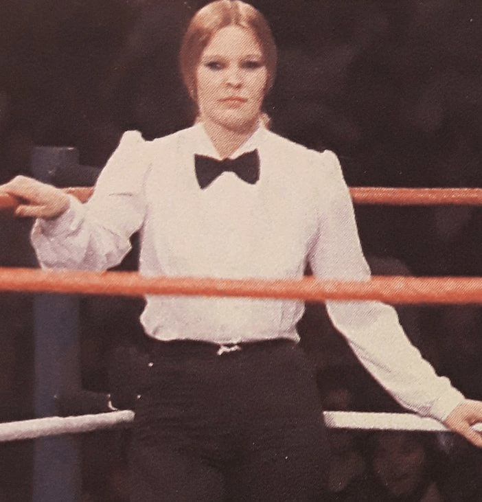 a woman in a tuxedo stands in a boxing ring