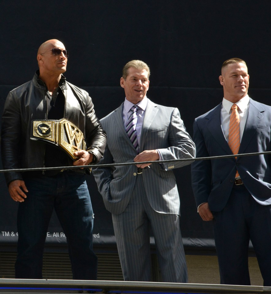 a man in a suit holds a wwe championship belt