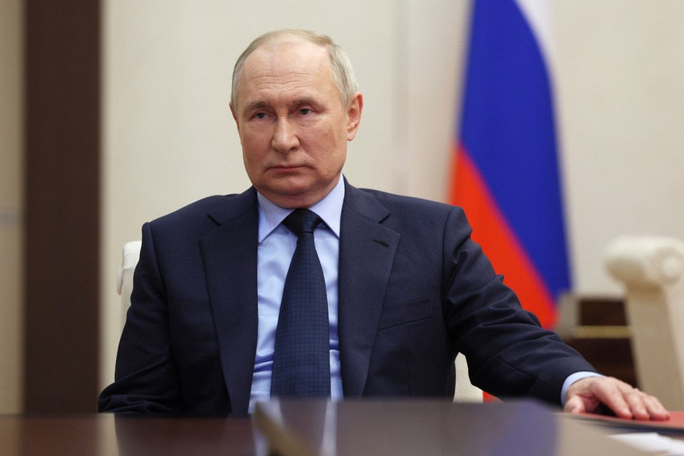 a man in a suit and tie sits at a table in front of a russian flag