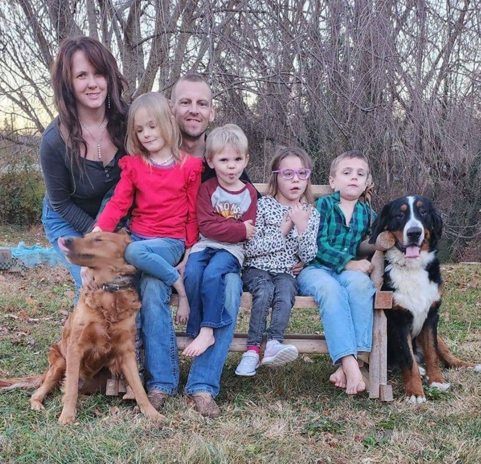 a family sits on a wooden bench with a dog