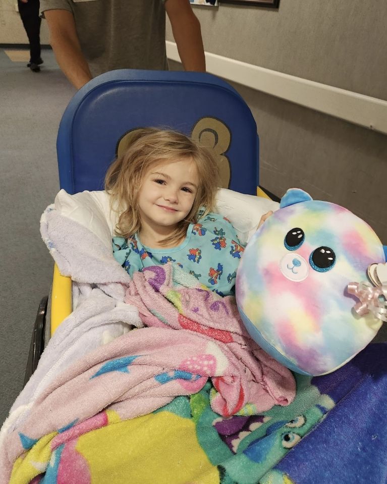 a little girl in a hospital bed holding a stuffed animal