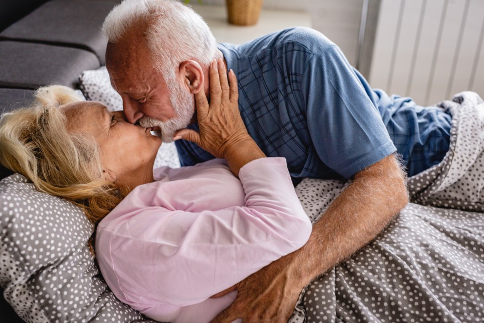 an elderly couple kissing on a bed under a blanket