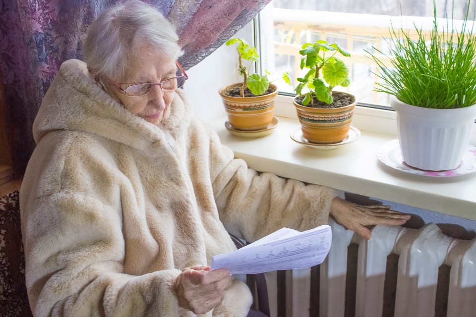 an elderly woman sits on a window sill reading a piece of paper