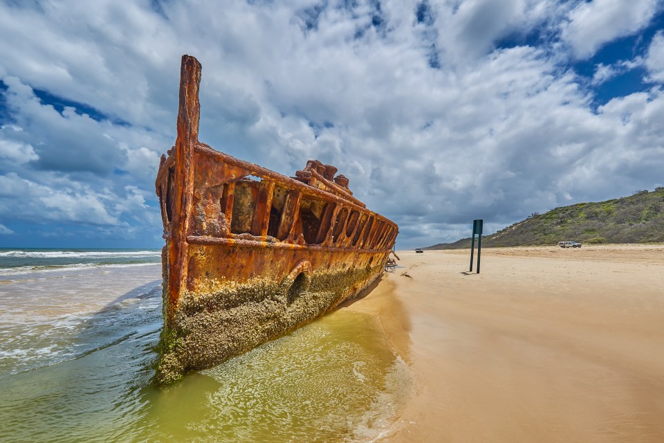 a rusty boat is sitting on a sandy beach