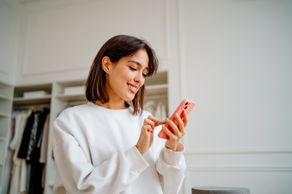 a woman in a white sweater is smiling while looking at her phone