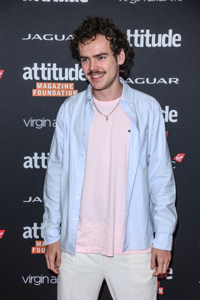 a man stands on a red carpet in front of a sign that says attitude magazine foundation