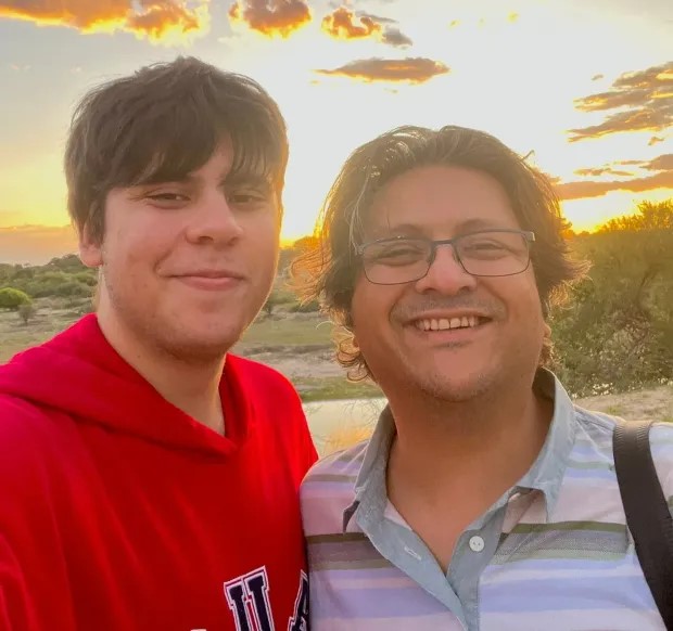 a man wearing glasses and a red hoodie is standing next to another man