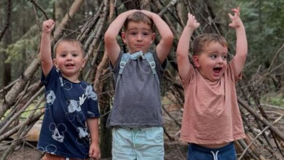 three young boys are standing next to each other in the woods with their hands in the air .