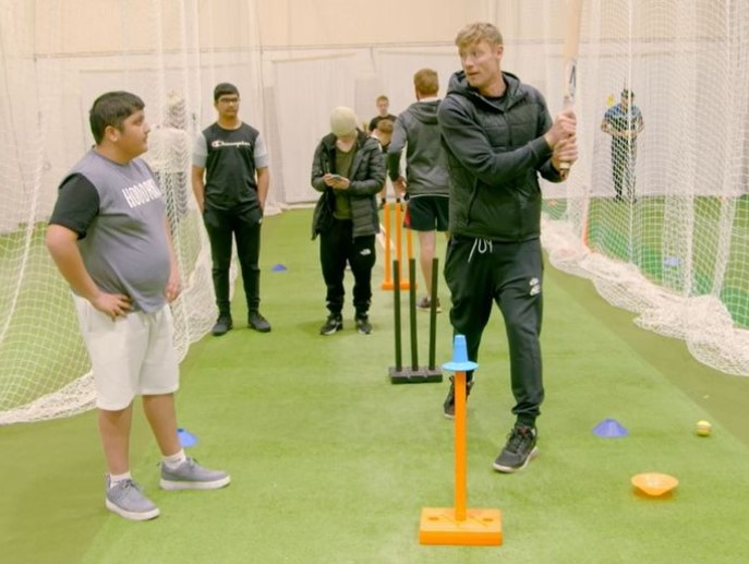 a boy wearing a champion shirt watches a man swing a bat