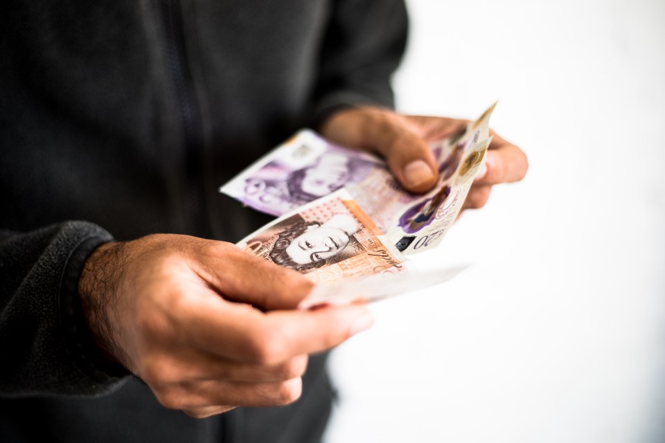 a man is holding a stack of british pound notes