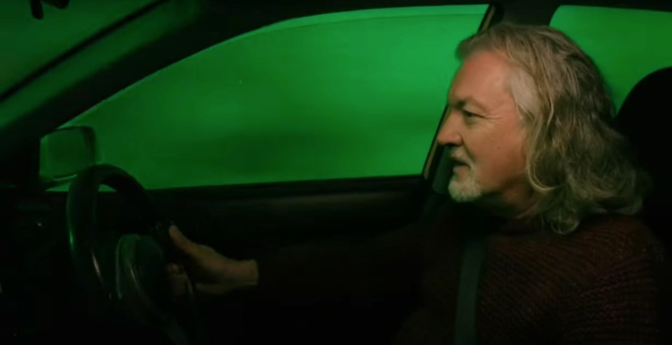 a man with long hair and a beard is driving a car with a green background