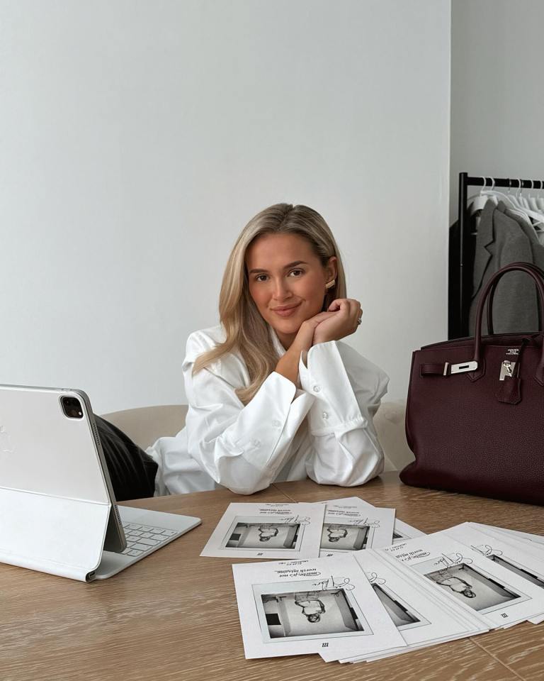 a woman sits at a desk with a laptop and a burgundy hermes bag