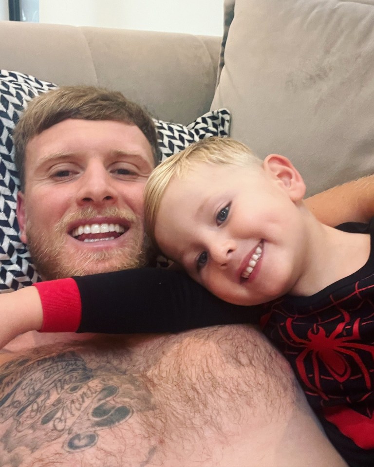 a man with a tattoo on his chest is laying on a couch with a little boy