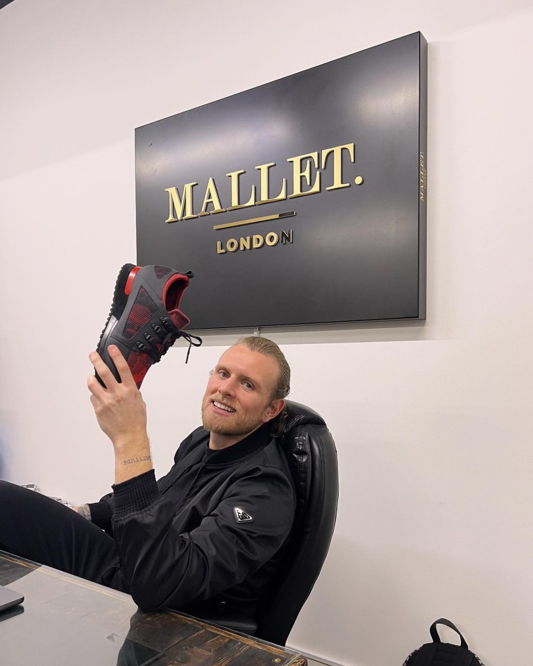 a man holding a shoe in front of a sign that says mallet london