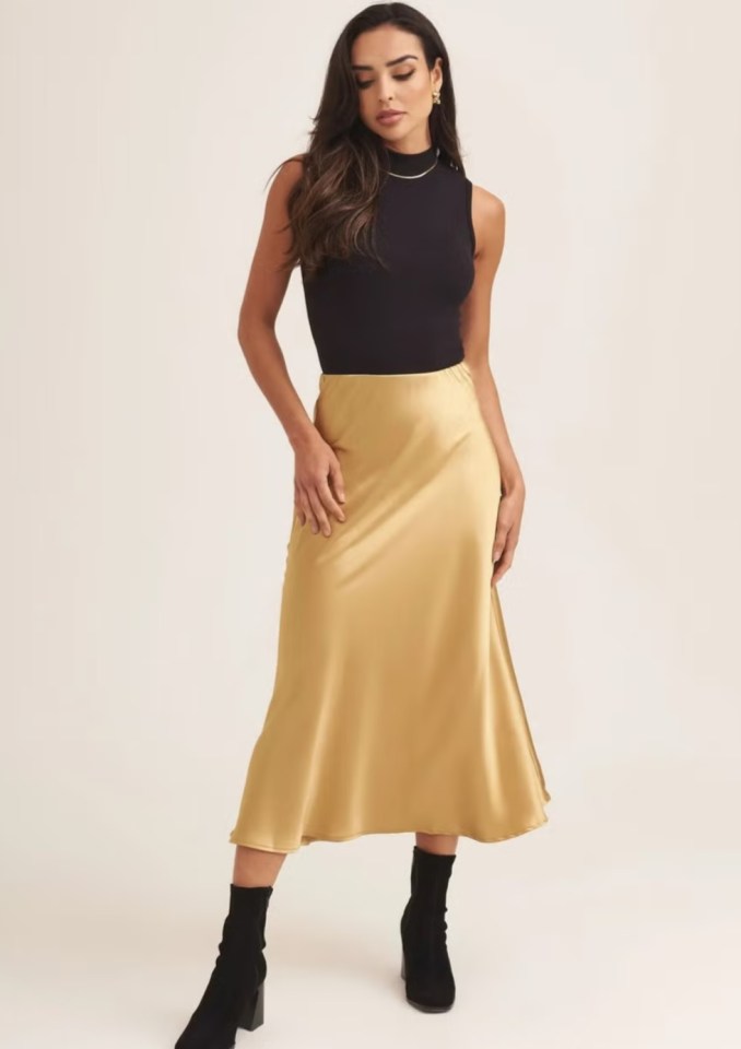 a woman wearing a black top and a gold skirt