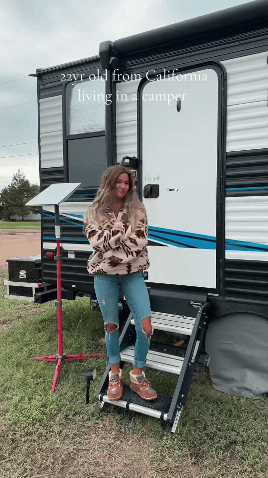 a woman standing in front of a trailer that says 22 yr old from california living in a camper