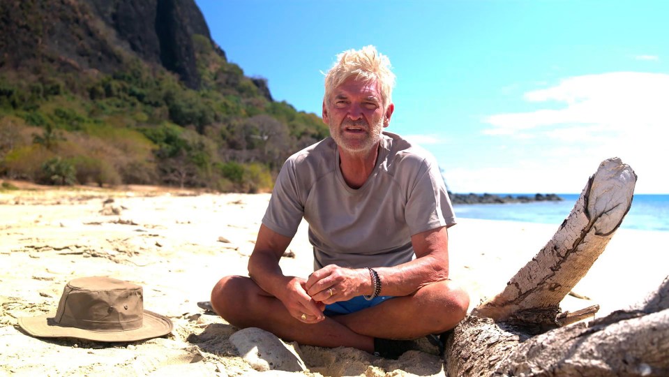 a man sits on a beach next to a hat