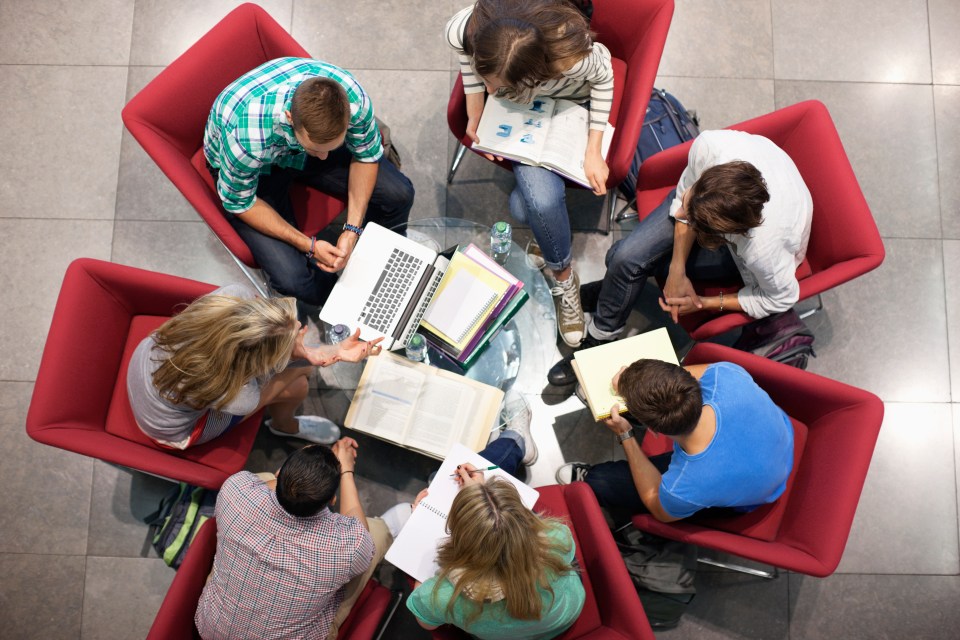 a group of students sit around a table with books and a laptop