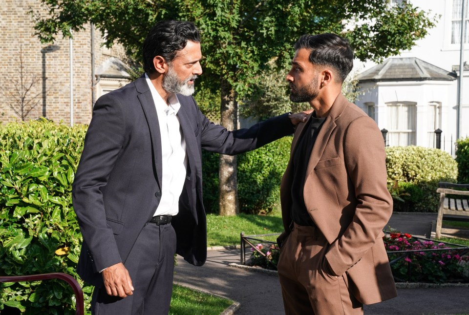 two men in suits are standing next to each other in a park