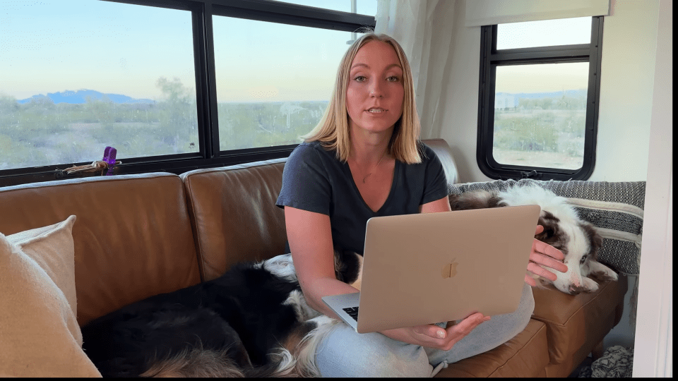 a woman sits on a couch with a dog and a laptop