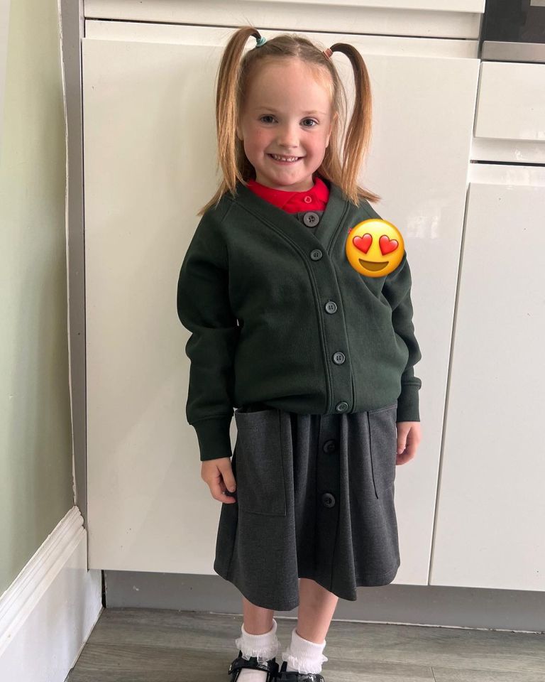 a little girl wearing a green cardigan and a grey skirt