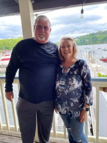 a man and a woman are standing next to each other on a balcony overlooking a body of water .