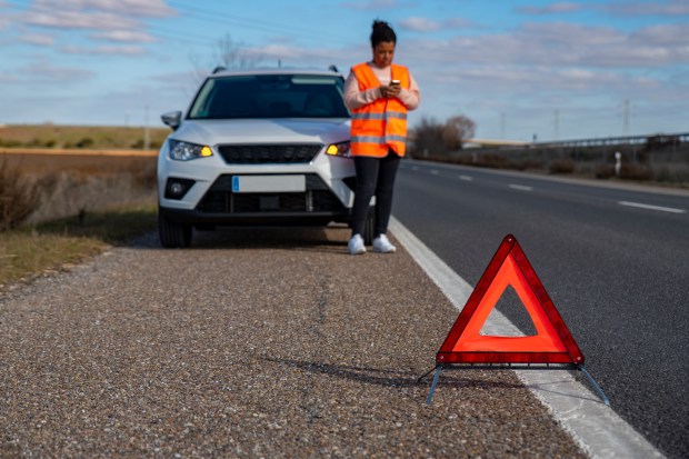 a woman standing next to a broken down car looking at her phone