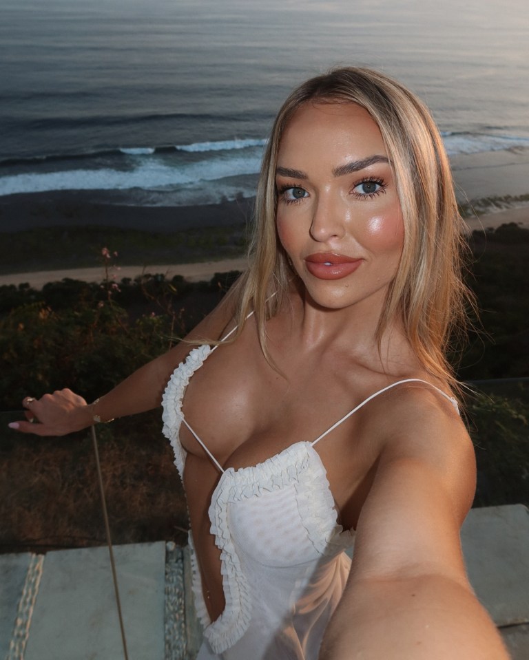 a woman in a white dress takes a selfie with the ocean in the background