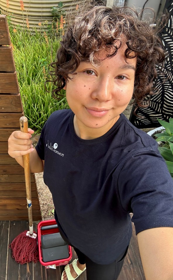 a woman is holding a mop and wearing a black shirt that says i am a survivor