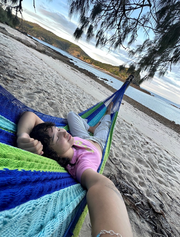 a woman in a pink shirt is laying in a hammock on the beach