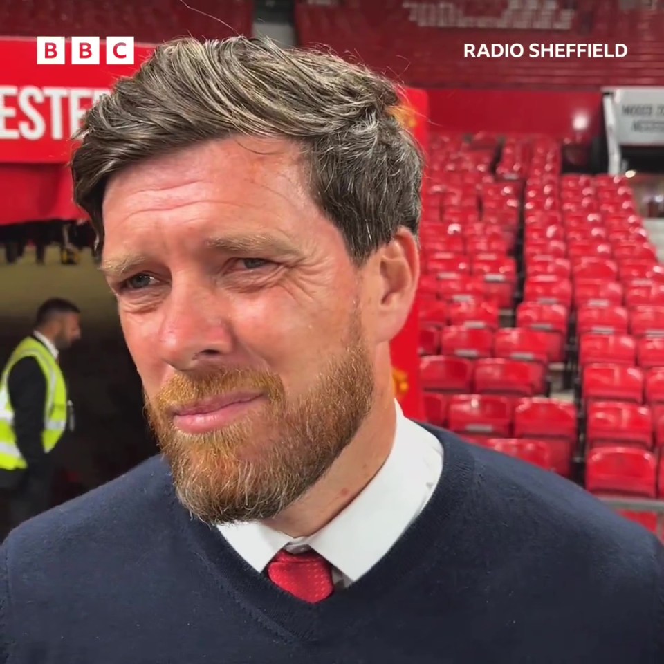 a man with a beard in front of a bbc sign