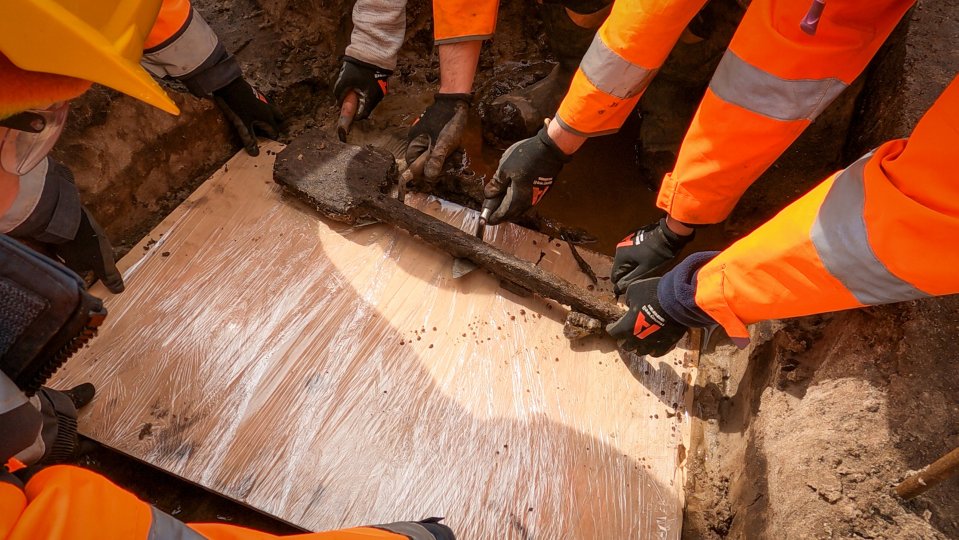 Archaeologists carefully lift the fragile spade from the ground on to a board