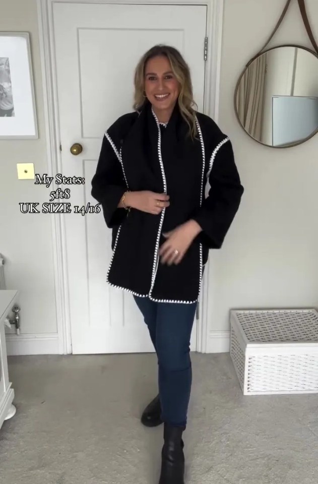 a woman standing in front of a door wearing a black coat with white trim