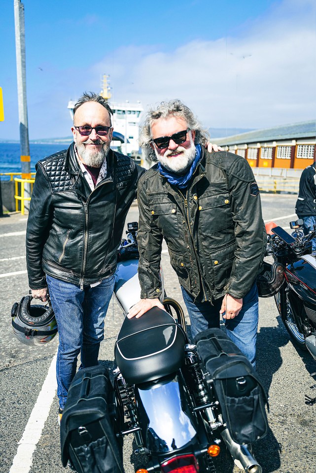 two men standing next to a motorcycle in a parking lot