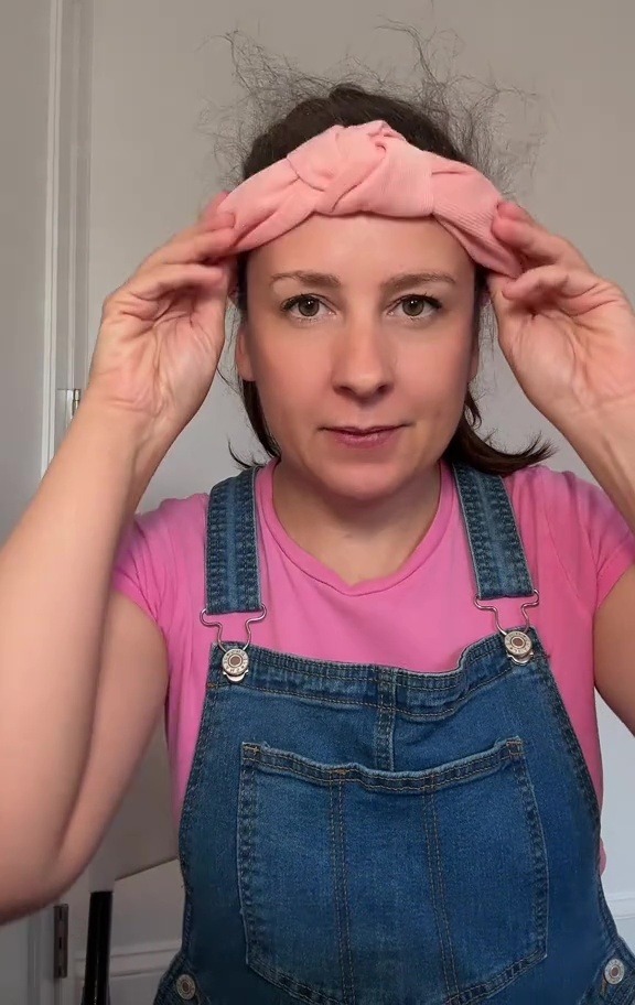 a woman wearing overalls and a pink shirt has a pink headband on her head