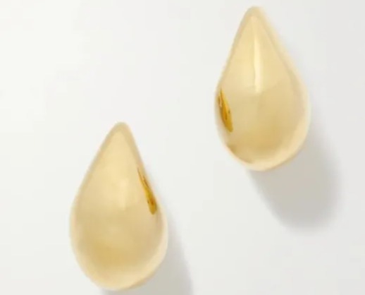 a pair of gold earrings are sitting on a white surface .