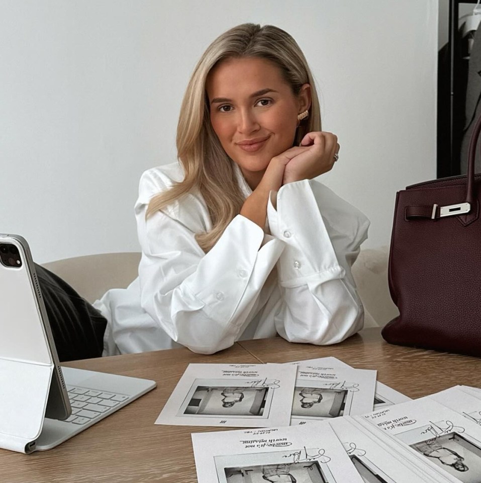 a woman sits at a desk with a laptop and a burgundy hermes bag