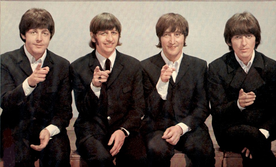 four men in suits are sitting next to each other and pointing at the camera