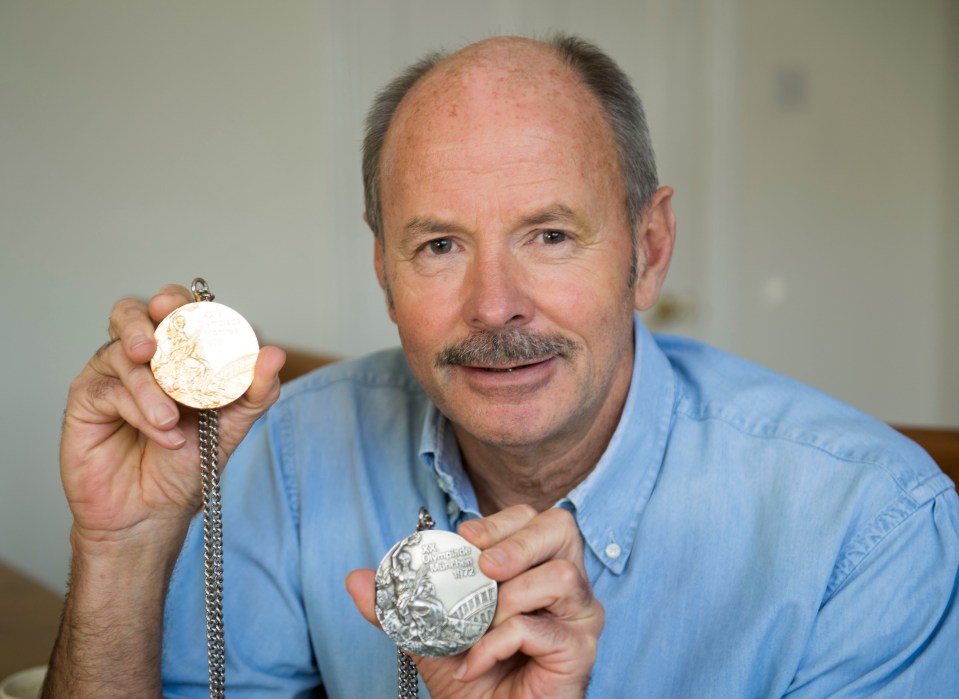 a man in a blue shirt holds up two medals one of which says ' athens olympics ' on it