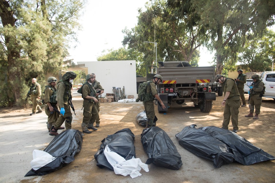 Israeli soldiers remove the bodies of civilians near the border with Gaza following last year's October 7 attacks