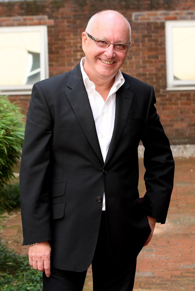 a man in a black suit and white shirt smiles for the camera