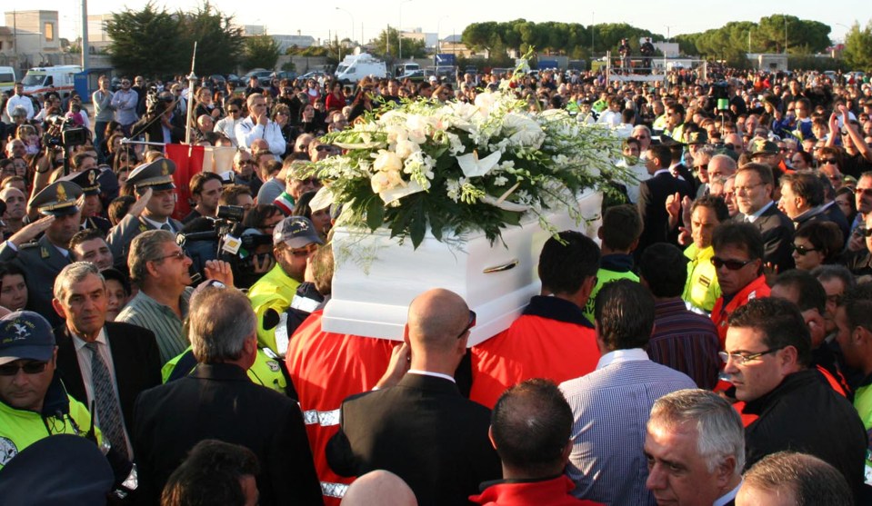 a crowd of people are gathered around a coffin with flowers on it