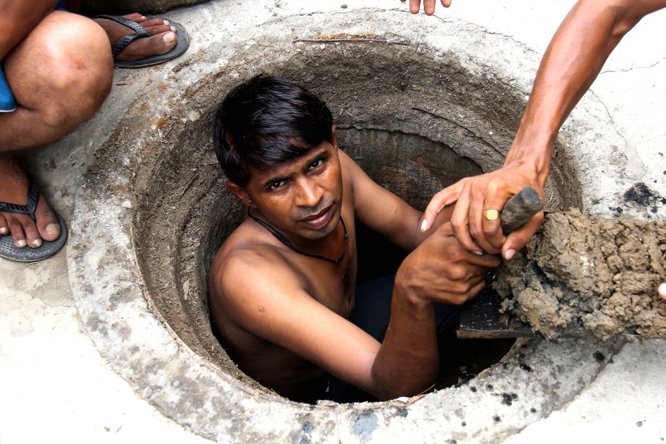 a shirtless man is looking out of a manhole