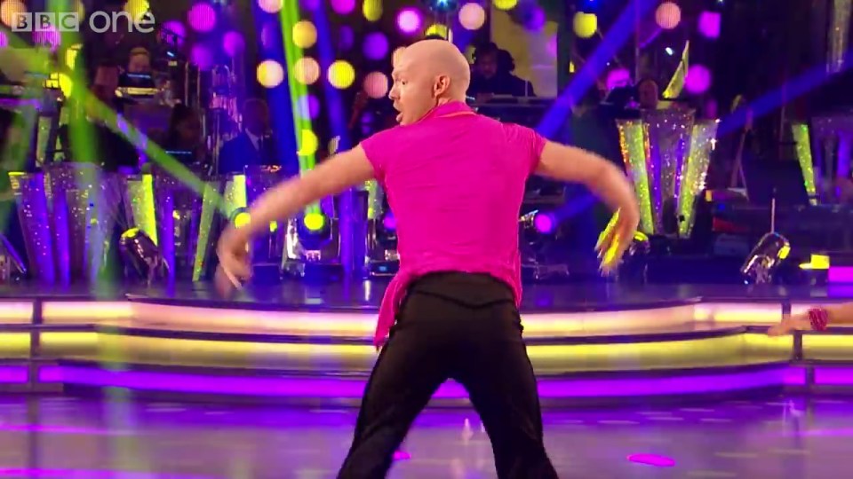 a bald man in a pink shirt is dancing on a stage