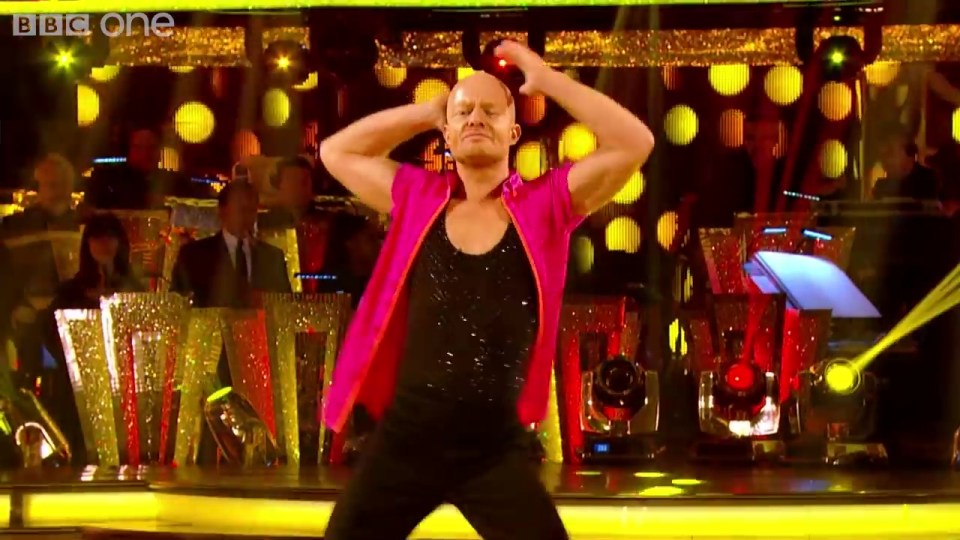 a man in a pink shirt is dancing in front of a bbc one logo