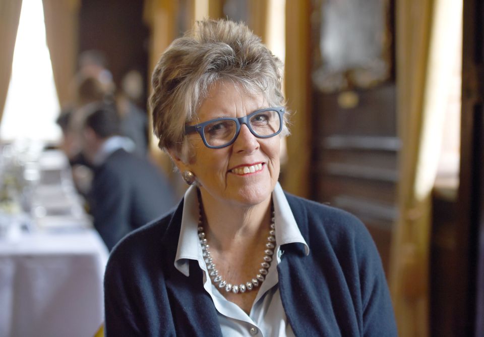 a woman wearing glasses and a pearl necklace smiles for the camera