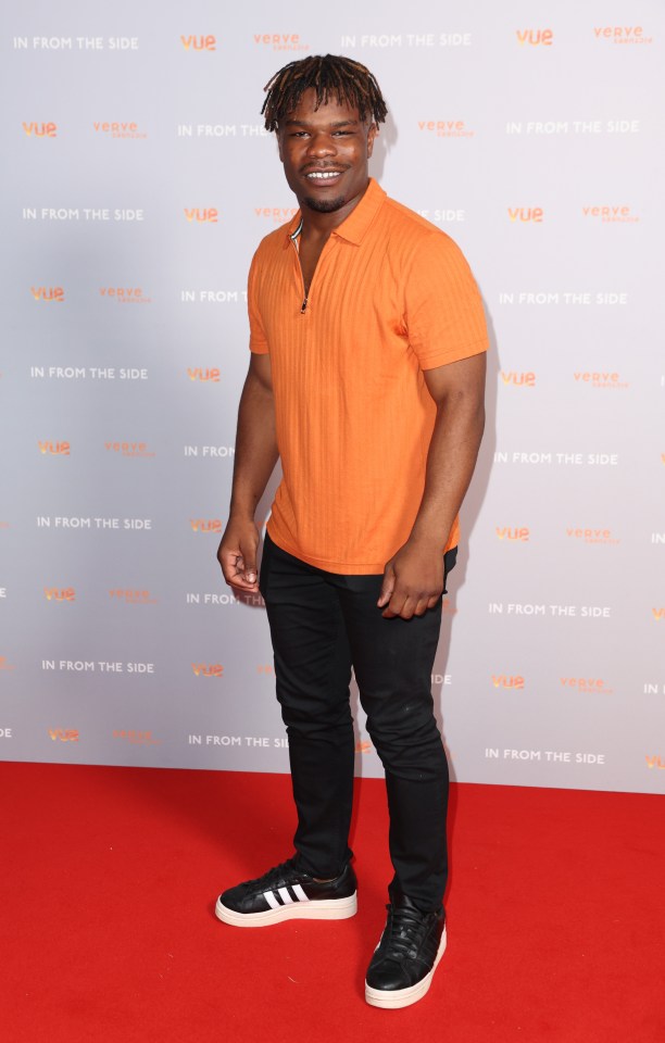 a man stands on a red carpet in front of a wall that says in from the side