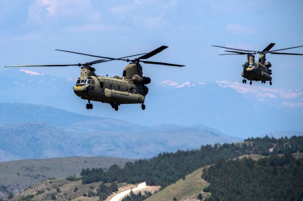 two military helicopters are flying over a mountain range