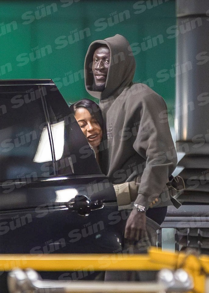 a man in a hoodie is standing next to a woman in a car with the sun newspaper behind them